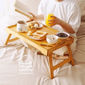 میز صبحانه تاشو چوبی روی تخت با چیدمان فنجان چای و کتاب